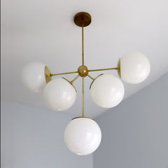 Art deco inspired chandelier with brass accents and white oversized globes by sazerac stitches - front view
