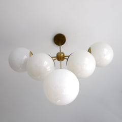 Art deco inspired chandelier with brass accents and white oversized globes by sazerac stitches - angled view