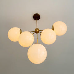 art deco inspired brass and white globe large chandelier lit up from the bottom.