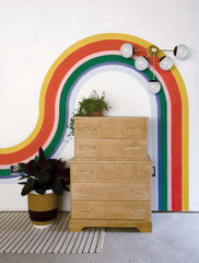 Rainbow mural, wood dresser, big rubber plant, and modern sconce by Sazerac Stitches