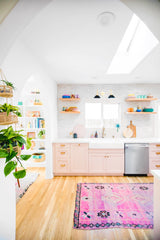 bright kitchen remodel with white handmade tile, pink cabinets, wood floating shelves, and black and brass sconce
