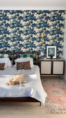 Wallpapered bedroom with blue floral wallpaper, midcentury modern style platform bed and sidetables, traditional style brass bedside sconces, and a pink oriental style runner rug.