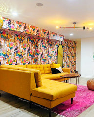Colorful and retro living room with a yellow sofa, tropical toucan wallpaper, and a pink overdyed rug