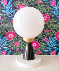 Black and white colorblocked lamp against a pink, green, blue, and navy wallpaper in a floral design