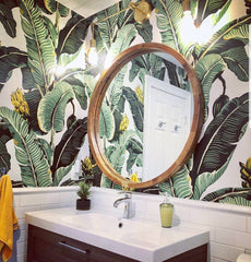 tropical themed bathroom wallpaper with a round mirror and a brass Magazine Sconce by Sazerac Stitches