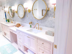 Girly pink bathroom with dramatic brass and gold wall sconces and circular mirrors
