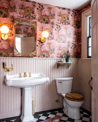 Maximalist pink floral bathroom with beadboard, black and white tile floors, pedestal sink, brass accents, and a vintage wood inlay mirror in Vanessa Carlton's bathroom