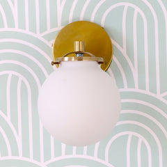 Brass wall sconce with white glass on a mint and white art deco inspired wallpaper