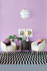 purple living room with white boucle chairs, rainbow gumball chandelier, and a cream and gold table lamp on an antique end table