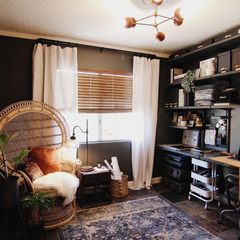 Boho dark office with mid century modern chandelier, black walls, and hints of natural elements like wood blinds, rattan chair, and woven seagrass basket.  The entire space is grounded with a vintage style rug.  The jewelry for the room is the terra cotta and brass mid century modern inspired chandelier by sazerac stitches