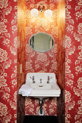 red floral bathroom with chrome wall sconce and white porcelain vanity sink