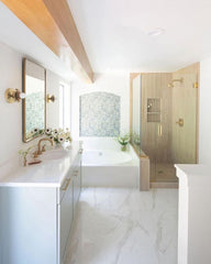 Large masterbathroom renovation with white marble floors, marble countertops, wood beam, wood like shower, large tup, and brass hardware and accent lighting.