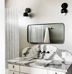 Black and white bathroom renovation with marble countertop, rectangular mirror, white stacked subway tile, and black mid century modern style sconces