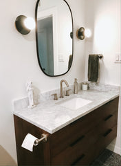 Neutral bathroom remodel with marble, dark wood, and olive wall sconces