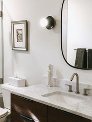 Neutral bathroom remodel with marble, dark wood, and olive wall sconces