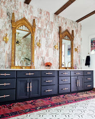 Antique style bathroom with pink marble tile, geometric floor tile, navy cabinets, and harry potter mirrors