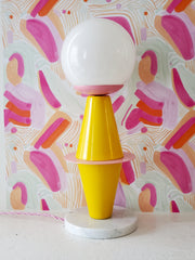 Yellow and pink table lamp with a marble base and glass globe on pink and orange watercolor wallpaper