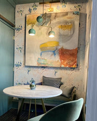 Kitchen nook with floral wallpaper, modern wall art, marble pedestal table, and a green and brass modern chandelier
