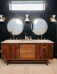 mid century modern bathroom with a converted cabinet, black tile, and cream and brass Clancy wall sconces