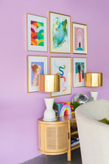 Colorful art gallery on pastel purple walls with a natural wood credenza and cream and brass table lamps