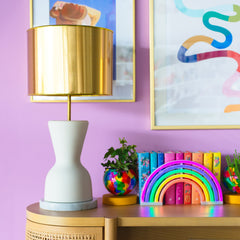 White Ceramic Lamp with a Gold Shade and a Marble base in a colorful lilac living room with rainbow art, rainbow books, and a rainbow planter