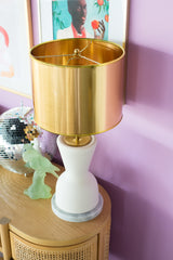Cream and marble table lamp with brassy gold lamp shade on a pale wood credenza in colorful and bold living room with pastel purple walls
