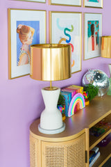 Colorful art gallery on pastel purple walls with a natural wood credenza and cream and brass table lamps