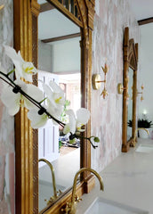 Brass adn copper wall sconce with antique style mirrors, marble tiled wall, and brass faucets in a bathroom