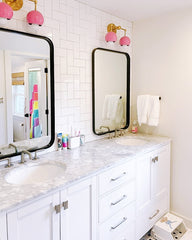White bathroom with black and white accents and mid century modern inspired wall sconces n pink and brass